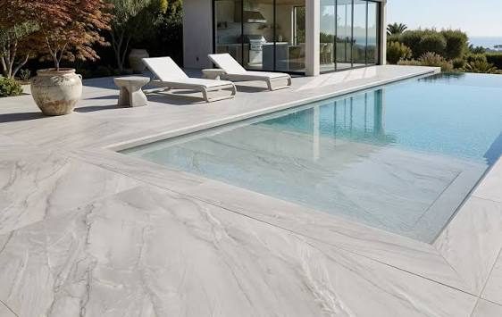 Light stone-look pool deck beside an infinity pool